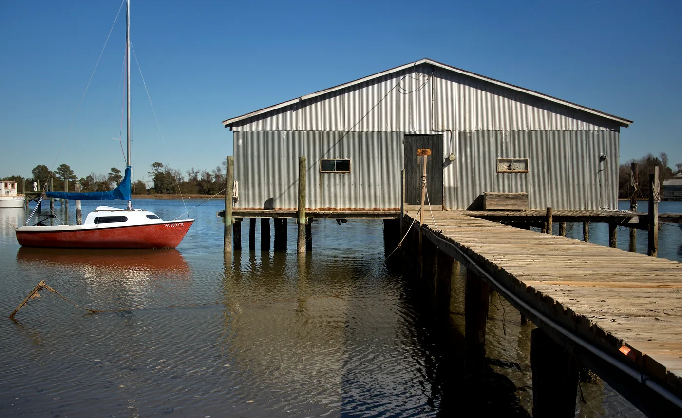 A boathouse, a dock and a sailboat on Urbanna Creek in the evening light